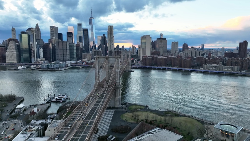 NYC, USA - APR 14, 2022: aerial following Brooklyn Bridge to American flag and Manhattan skyline East River in New York City.