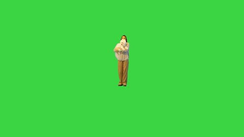 Smiling glamorous woman in white holding white fluffy dog while walking on camera on a Green Screen, Chroma Key.