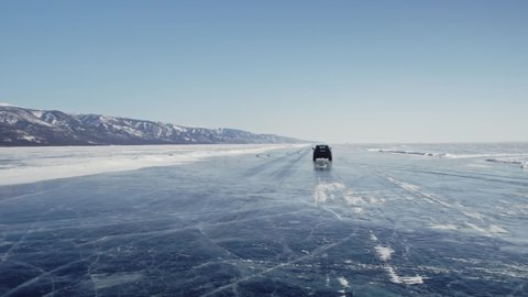 A dark car quickly drives through the winter on snowy ice on Lake Baikal in the background of the mountain