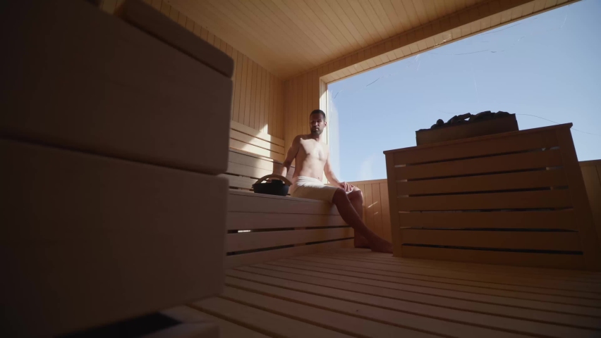 Handsome young man pouring water onto hot stone in the sauna