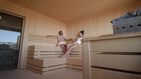 Handsome young couple relaxing in the sauna and watching winter forest through the window