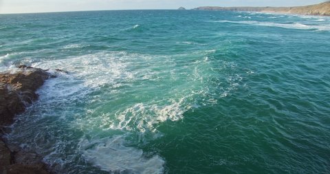 View of Foamy Turquoise Green Waves Splashing Over Coastal Rocks from Cliffside, Cornwall - slow motion