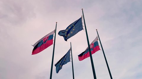 Slovakia and European Union flags next to each other fluttering in wind on flagpole, slow motion low angle view