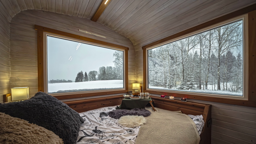View of nicely decorated and cozy bedroom in a wooden vacation cabin in a snow covered winter landscape at daytime in timelapse.