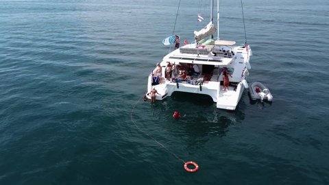 Phuket, Thailand, 19, December, 2020:
Sailing catamaran in the sea at anchor, drone view, many people are resting on board or swimming near the boat