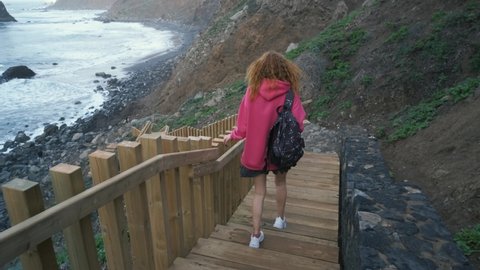 Young woman tourist goes down the long stairs to the famous volcanic black sand beach Benijo in the north of Canary island Tenerife