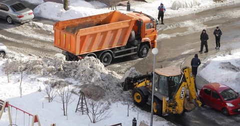 Moscow, Russia February 27, 2021. Winter snow removal from sidewalks. A mini tractor shovels snow and loads it into a bucket. View from above.