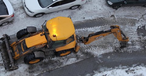 Moscow, Russia February 27, 2021. Winter snow removal from sidewalks. A mini tractor shovels snow onto the side of the road. View from above.
