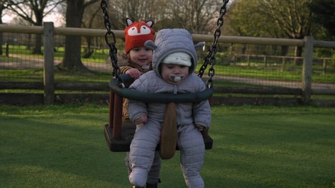 Funny Little Preschool Chubby Girl Older Sister Rides Younger Newborn Infant Brother Boy On Swing. Baby Playing On Playground. Kids Entertainment, Childhood, Child Development, Happy Family Concept