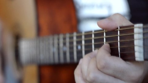 closeup young caucasian man indoors playing acoustic guitar with focus on left hand on fretboard, copy space, music concept.