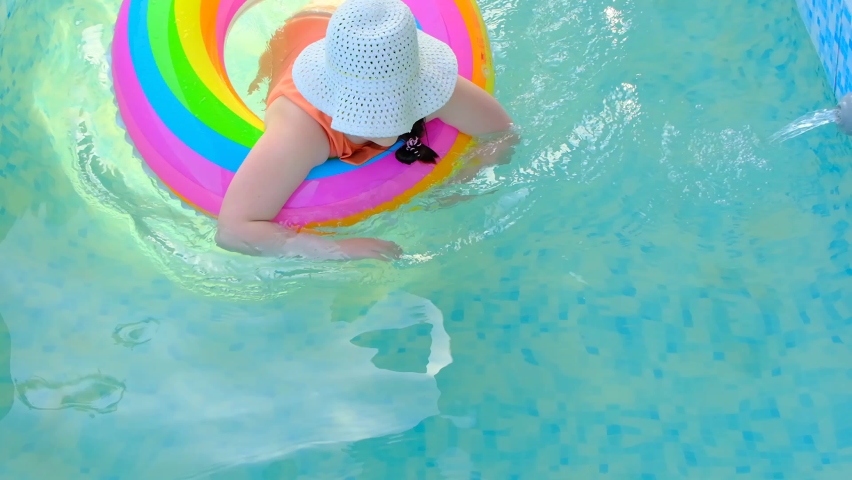 Girl with a rainbow inflatable ring in the pool.slow motion. Child swims in the swimming pool.Summer time and holidays. 4k footage