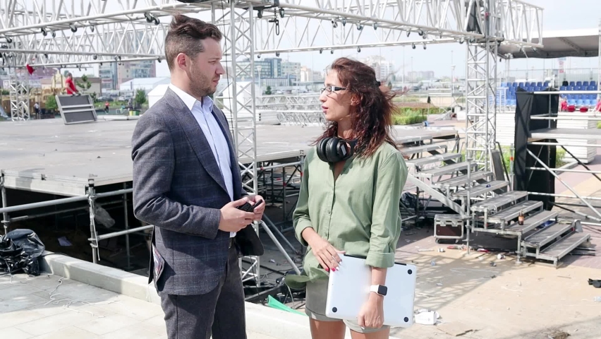 Event managers discuss stage construction. Installation of stage equipment and preparing for a live concert open air. Event manager portrait. Summer music city festival. Teamwork.