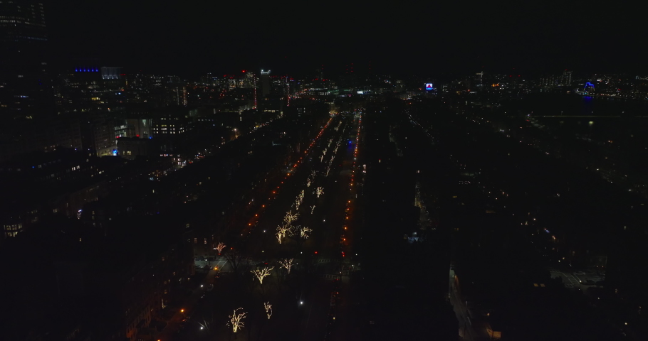 Forwards fly above night city. Wide straight street lined by street lights and with illuminated trees in middle. Boston, USA
