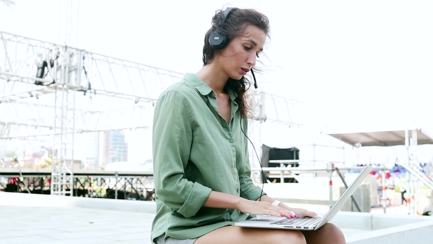 Technical support manager chat with a client. 
Installation of stage equipment and preparing for a live concert open air. Summer music city festival. Woman work with laptop.