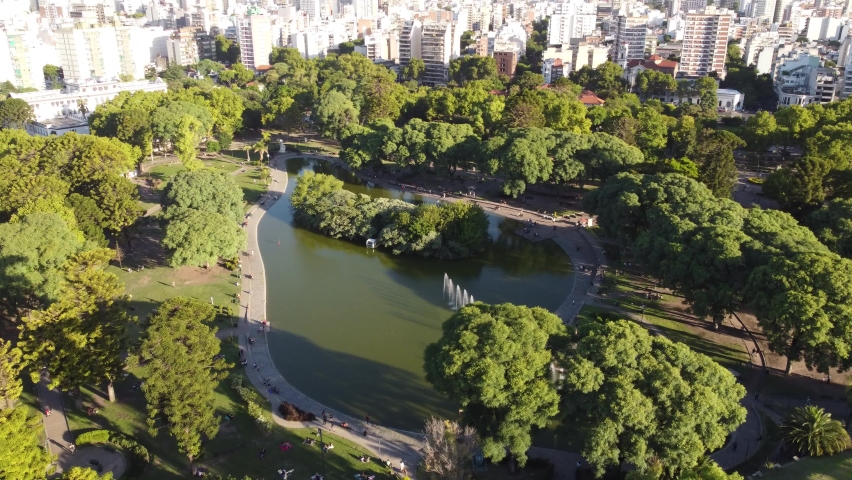 Argentine people relaxing at Centenario Park lake with Buenos Aires cityscape in background. Aerial tilt down Royalty-Free Stock Footage #1089532415