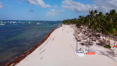 Sand beach full of sunbeds, boats on Caribbean sea, Bavaro resort in Punta Cana, Dominican Republic, aerial drone view, low flight