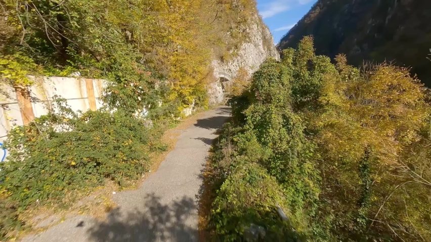 FPV drone extreme flight old serpentine asphalt highway antique tunnel near natural high mountain. Aerial view speed flying on road autumn nature wooden panorama cinematic sunny valley rocky terrain