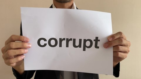 Frustrated asian male businessman professional crumpling paper with message "corrupt" word. Man in suit and tie having nervous breakdown furiously throwing away crumpled paper at work in office
