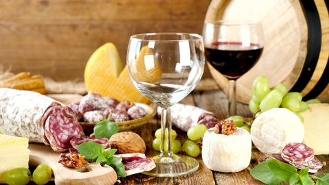  red wine pouring into a glass, cheese and salami composition