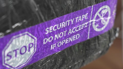 Close-up view 4k video of purple and white security tape with inscription - Security tape do not accept if opened isolated on black wrapped parcel. Home delivery from post office. Poland