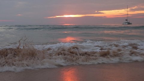 Sea Wave Water Foam Splash Washing Sandy Beach At Sunset. The yacht floats in the sea. Sundown Vacation Background.