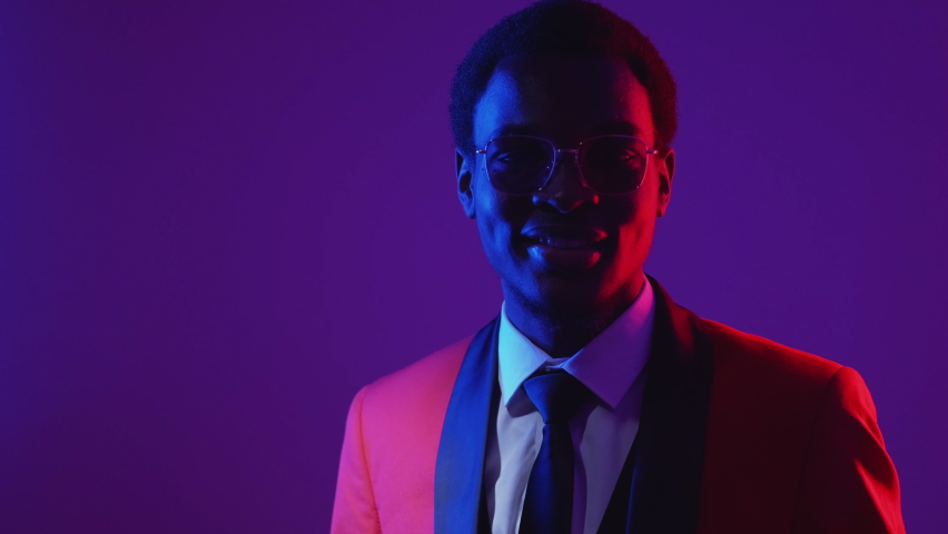 OK gesture. Consent agreement approval. Neon light smiling happy joyful man in elegant tuxedo suit glasses isolated on purple.