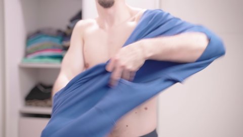 Headless nude male put on blue t-shirt in bedroom 4K
