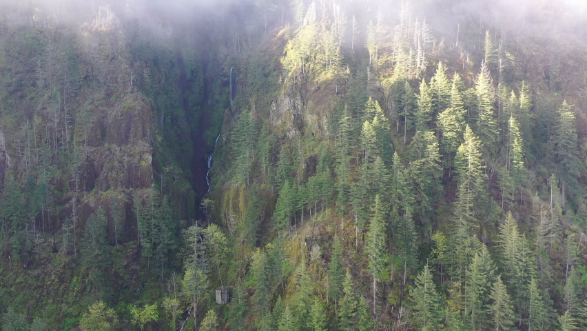 Low clouds drift over a scenic waterfall plunging over 500 feet into the Columbia River Gorge, Oregon. This narrow canyon, with the Columbia River flowing through it, separates Oregon and Washington.