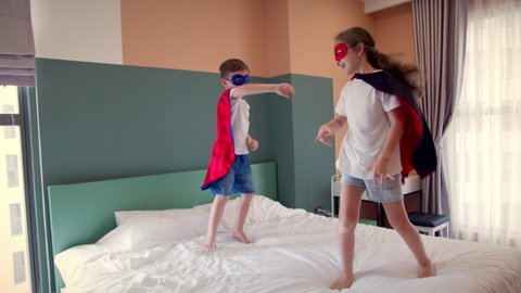 Girl and boy superheroes, are jumping in room on bed,in children's room, two children in red and blue Superman costume, Superheroes, brother and sister, play at home imagining they are superheroes.