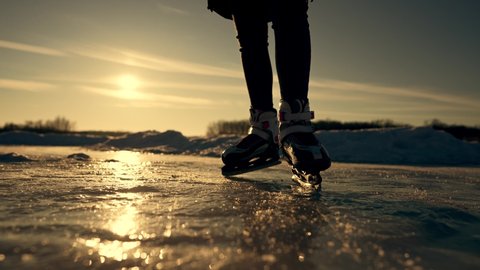 Silhouette of child in ice skates on frozen lake. Winner girl is skating. Sunset on the river in park. Happy girl in winter on ice in park. Child learns to skate. Silhouette of girl on lake at sunset