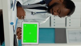 Vertical video: Physician holding digital tablet with horizontal greenscreen at consultation with pregnant woman. Male doctor using blank chroma key with isolated mockup template and copyspace. Tripod