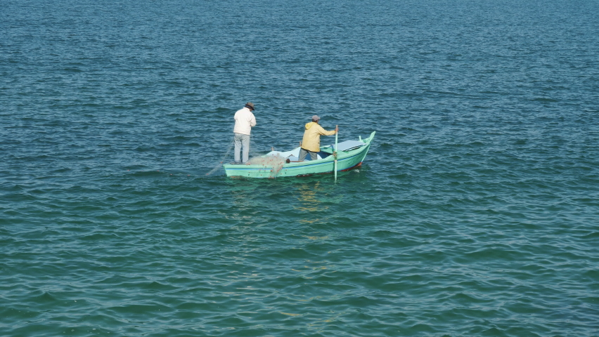 Fishermen on rowboat cast net into sea water. Poachers are engaged in fishing. Men standing in boat, waiting for fish catch. Fishers ship floating on waves. Fishery, lifestyle, hobby Royalty-Free Stock Footage #1089548135