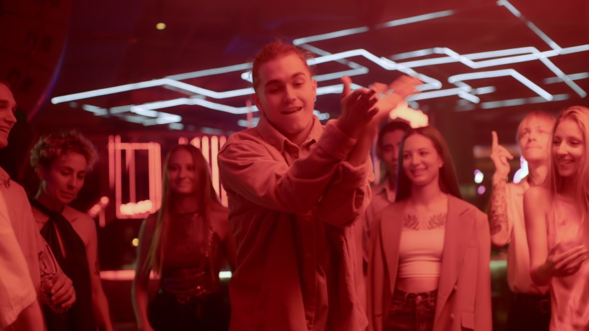 Group of young friends dances together in neon light of night club. Energetic playful moves in disco rhythm or hip-hop music. Partying joyful man at funky techno evening in bright multi-color shine | Shutterstock HD Video #1089548507