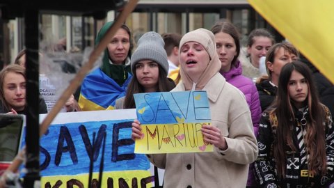Poland, Wroclaw, April 22, 2022: Crying girl with a yellow-blue poster save Mariupol. Rally of refugees in support of Ukraine. Diaspora and migrants
