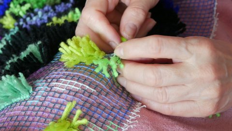Hand embroidered carpet. A woman using a special hook and thread embroiders a carpet with green threads. Handmade carpet embroidery. Women's hands create a pattern using multi-colored threads.