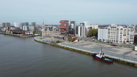  19 April 2022, Antwerp, Belgium : Green tug boat docked on the river Scheldt with Antwerp Loodswezen and MAS building in the background. Drone aerial view from above