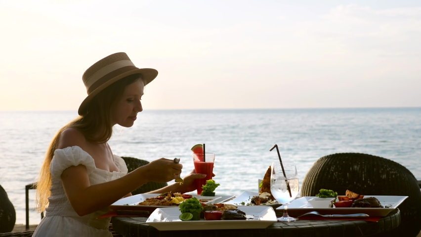 Young woman on holiday vacation enjoy her dinner with fruit watermelon cocktails in luxury resort restaurant on tropical beach with sea background. Beautiful girl chews tasty food in beachfront cafe. | Shutterstock HD Video #1089556893