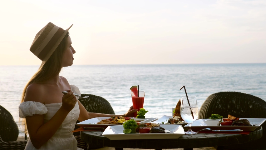 Young woman on holiday vacation enjoy her dinner with fruit watermelon cocktails in luxury resort restaurant on tropical beach with sea background. Beautiful girl chews tasty food in beachfront cafe. Royalty-Free Stock Footage #1089556893