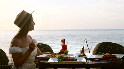 Young woman on holiday vacation enjoy her dinner with fruit watermelon cocktails in luxury resort restaurant on tropical beach with sea background. Beautiful girl chews tasty food in beachfront cafe. ஸ்டாக் வீடியோ