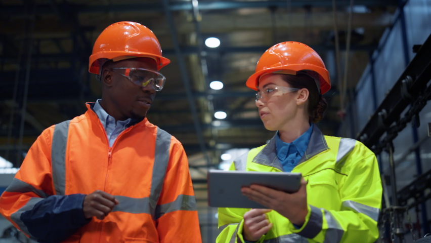 Workers partners holding tablet computer walking at modern manufacturing factory. African american man industrial specialist discussing project work with woman engineer warehouse. Team work concept. Royalty-Free Stock Footage #1089558327