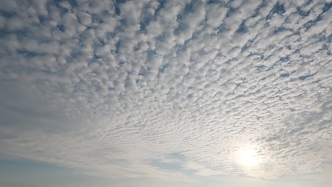 Rolling patches of clouds, time lapse shot of sky at sunny evening. Curling cirrocumulus clouds move slightly, bright sun quickly move down. Tropical island nature scenery