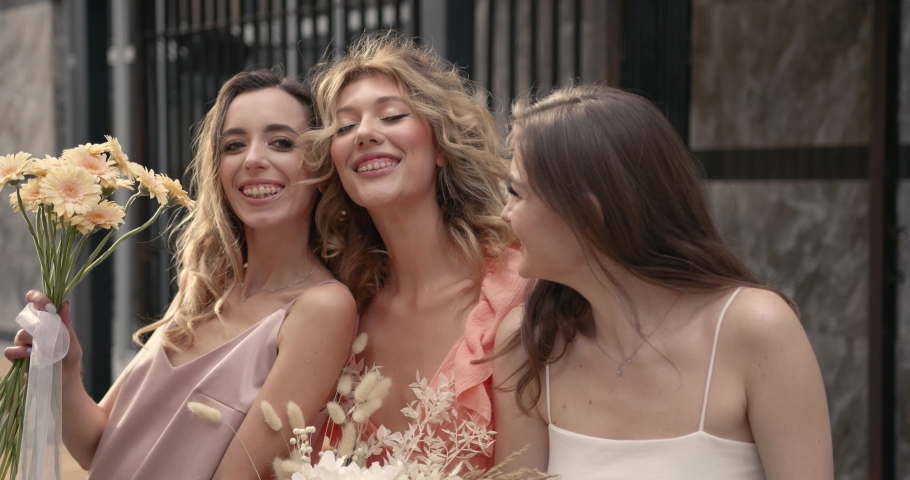 Three hapy ladies with bouquets posing in the city