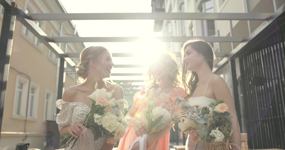 Three hapy ladies with bouquets posing in the city