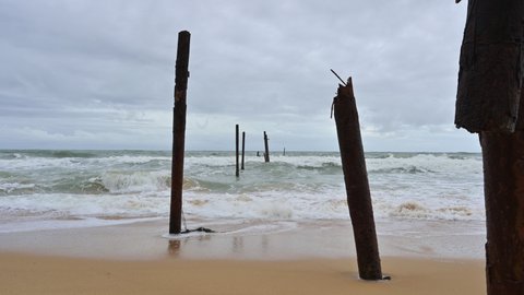 Big wave hitting a decay wooden bridge on the beach in stormy weather at Pilai beach, Phang nga, Thailand
