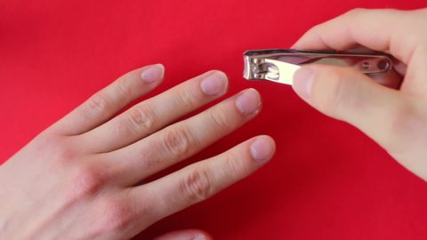 Looking down at a person clipping their nails with a metal nail clipper on a red background