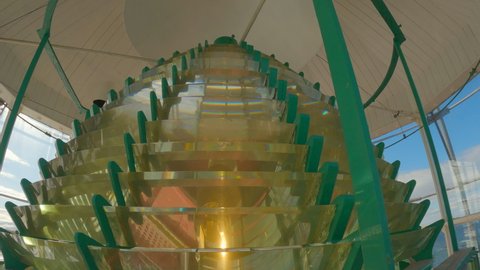Slow tilt shot, indoors looking up at the top of the fresnel lens of a lighthouse in motion with the lamp on during the day