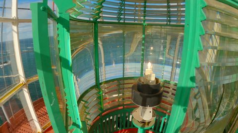 Static inside shot of the lantern room of a lighthouse during a bright sunny day with the fresnel lens moving by the lamp light