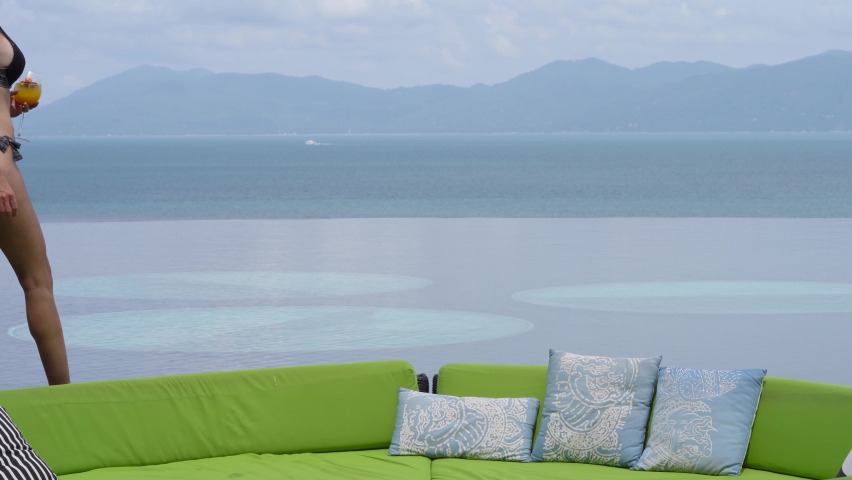 Caucasian Woman In Sexy Bikini Holding A Glass Of Lemonade Walking Around A Floating Sofa In An Island Hotel Pool In Koh Samui, Thailand. - Medium Shot