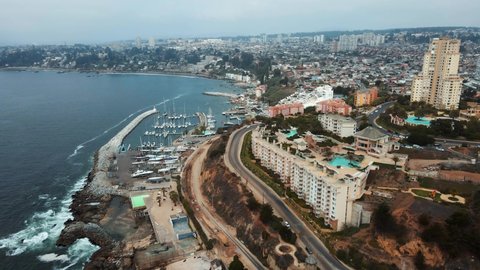 Aerial orbit of pier with sailboats parked in Negra beach area near the sea and Concon resorts and buildings on an overcast day, Chile