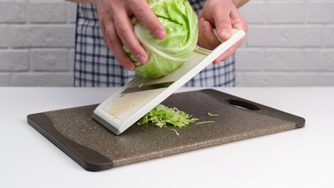 Male hand slicing green cabbage for a salad with a grater.